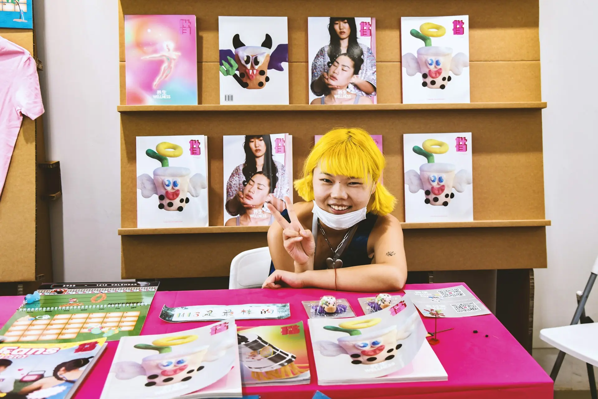jeune fille avec cheveux jaunes souriant devant magazines enfants colorés exposés